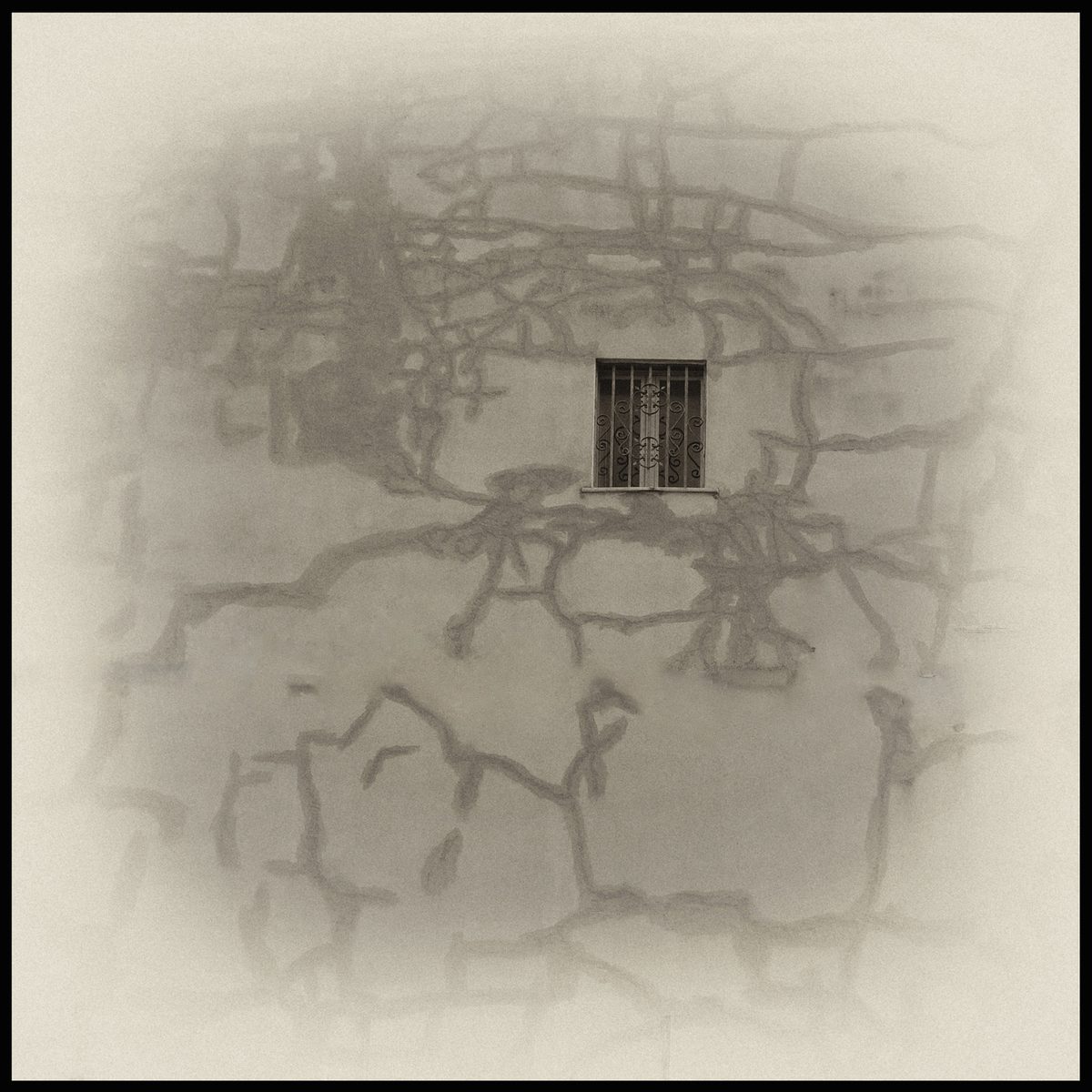 Weathered wall with cracks and a small barred window in a symbolic photograph by Augusto De Luca
