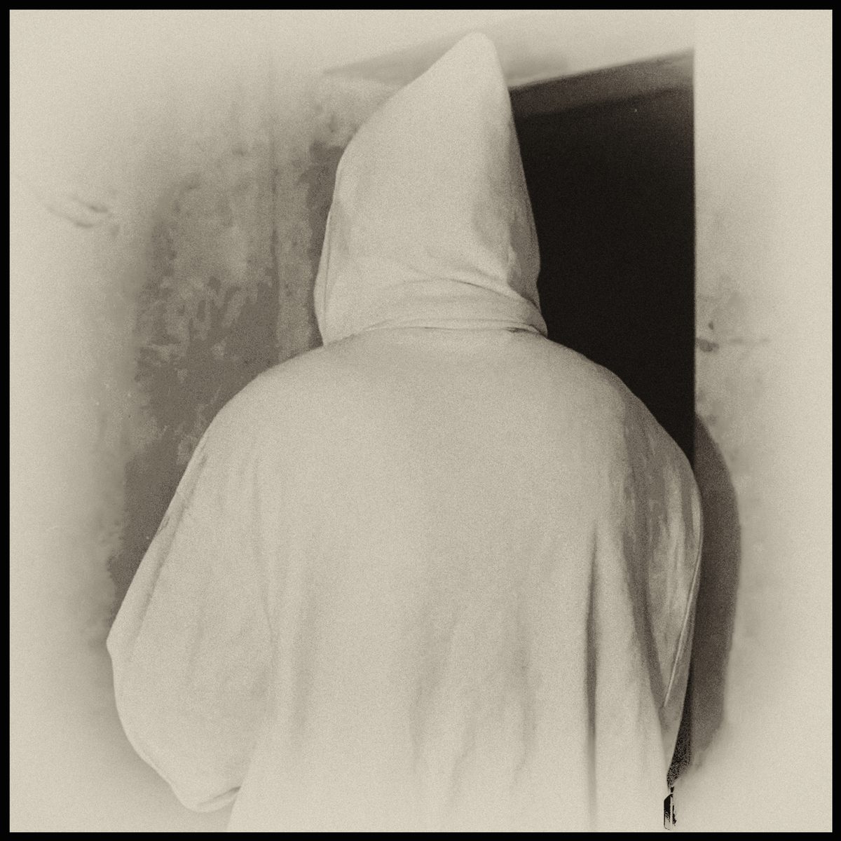 Hooded figure dressed in white standing with their back to the viewer in a surreal photograph