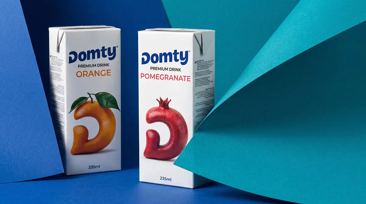 DOMTY orange and pomegranate juice cartons displayed against layered blue and turquoise paper backgrounds
